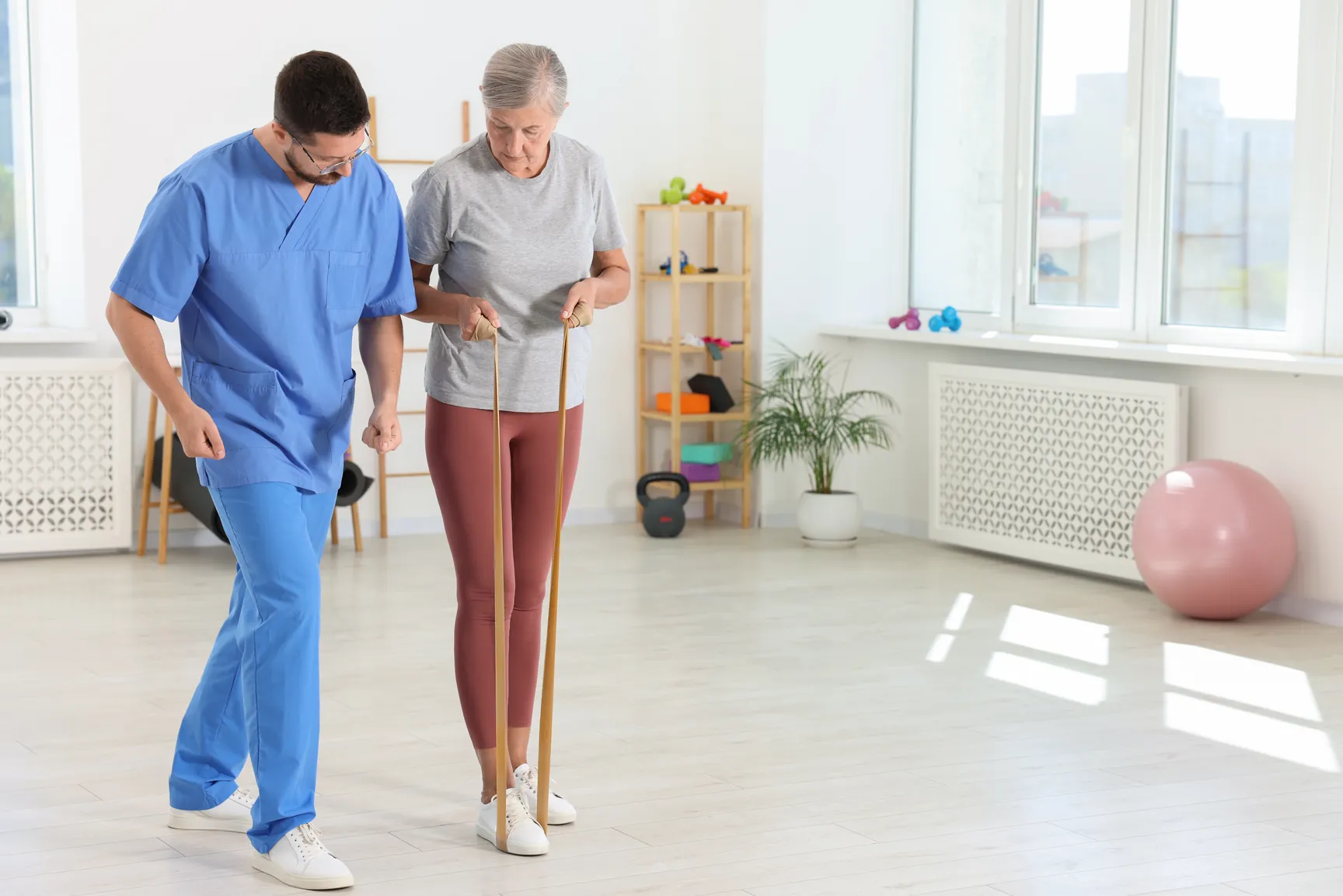 Physiotherapist guiding an older patient through a standing resistance band exercise