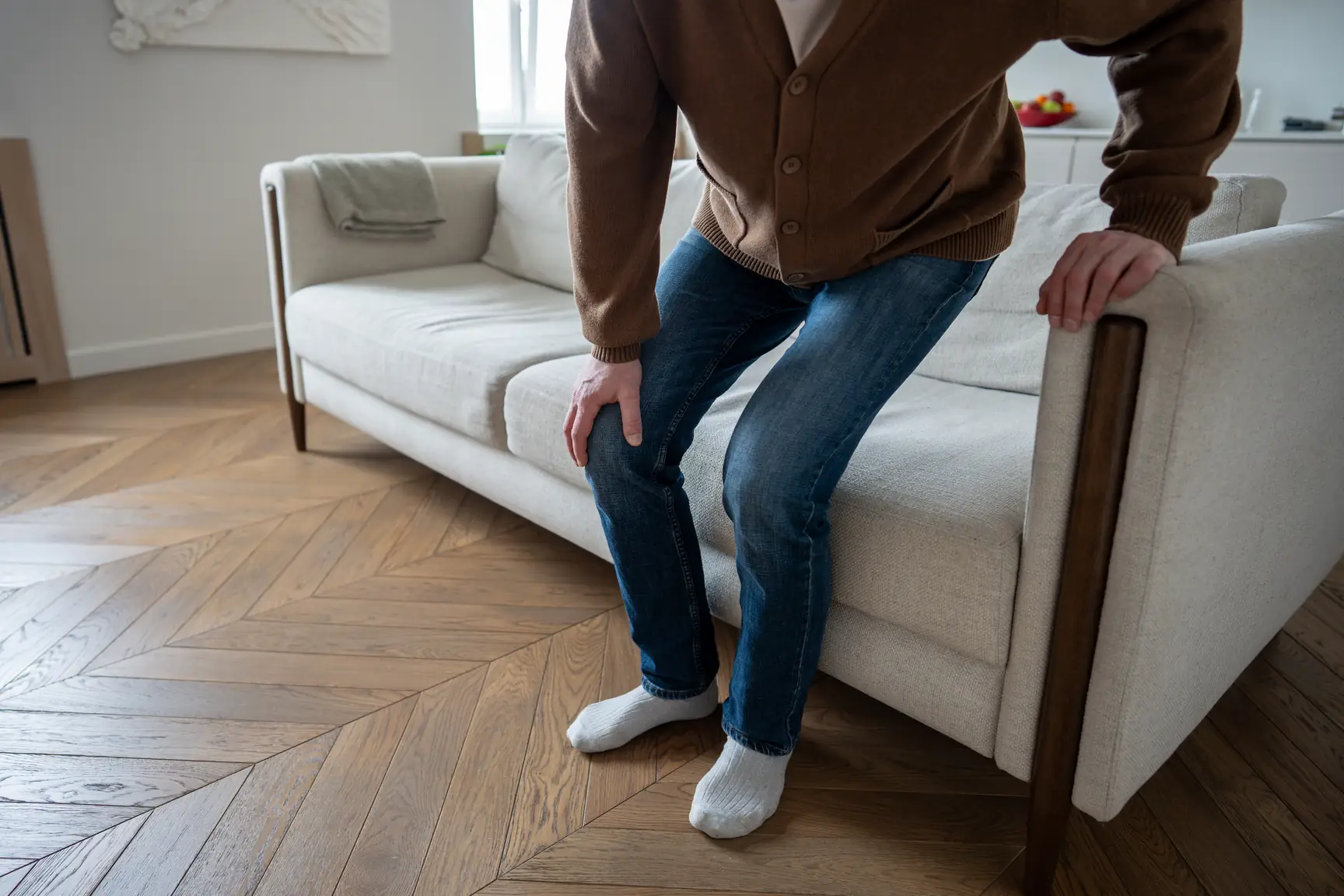 Man sitting on a sofa holding the back of his leg in pain
